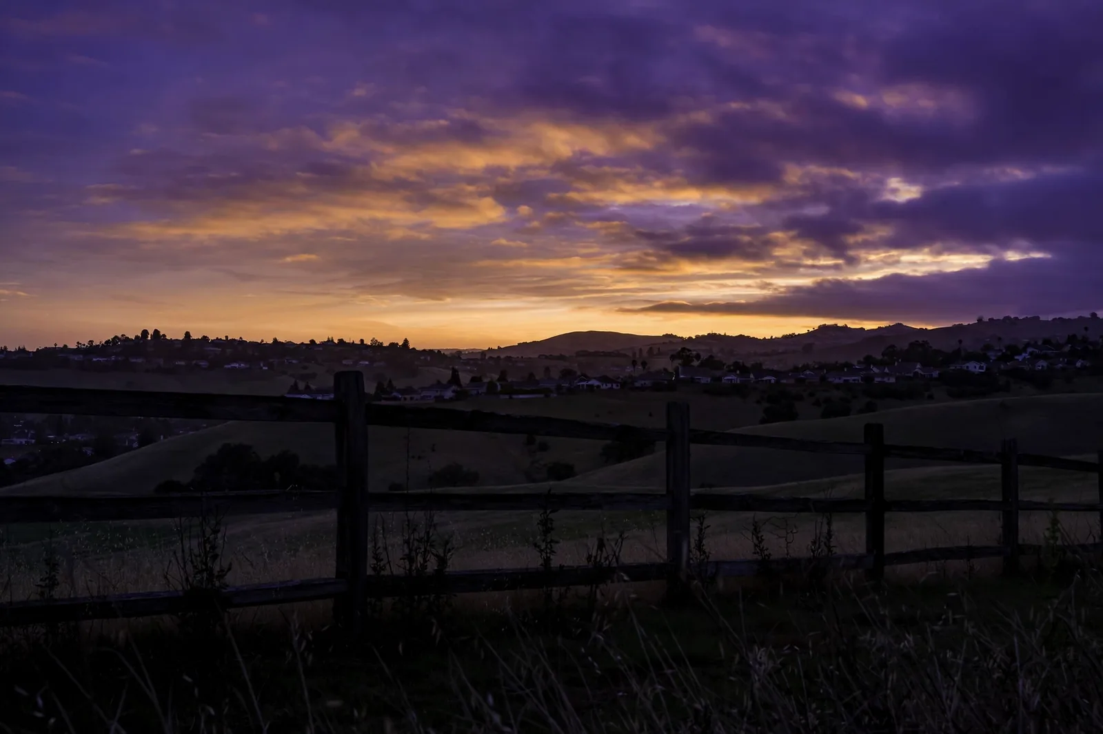 A fence line in silhouette at dusk under a violet sky